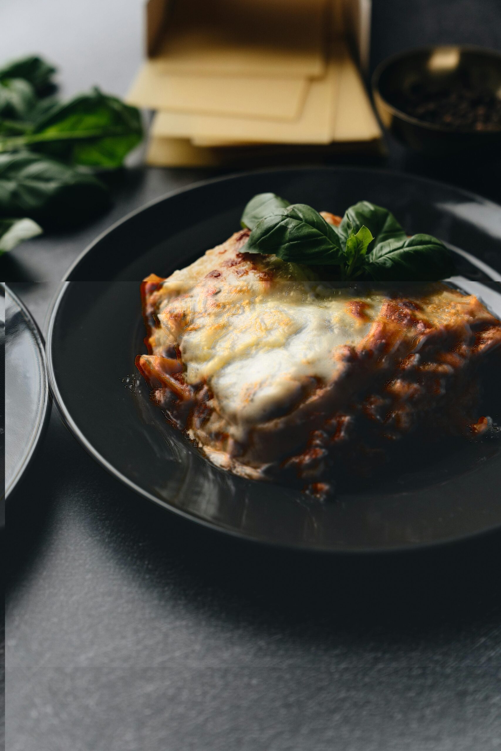 lasagna su un piatto nero con foglia di basilico sopra